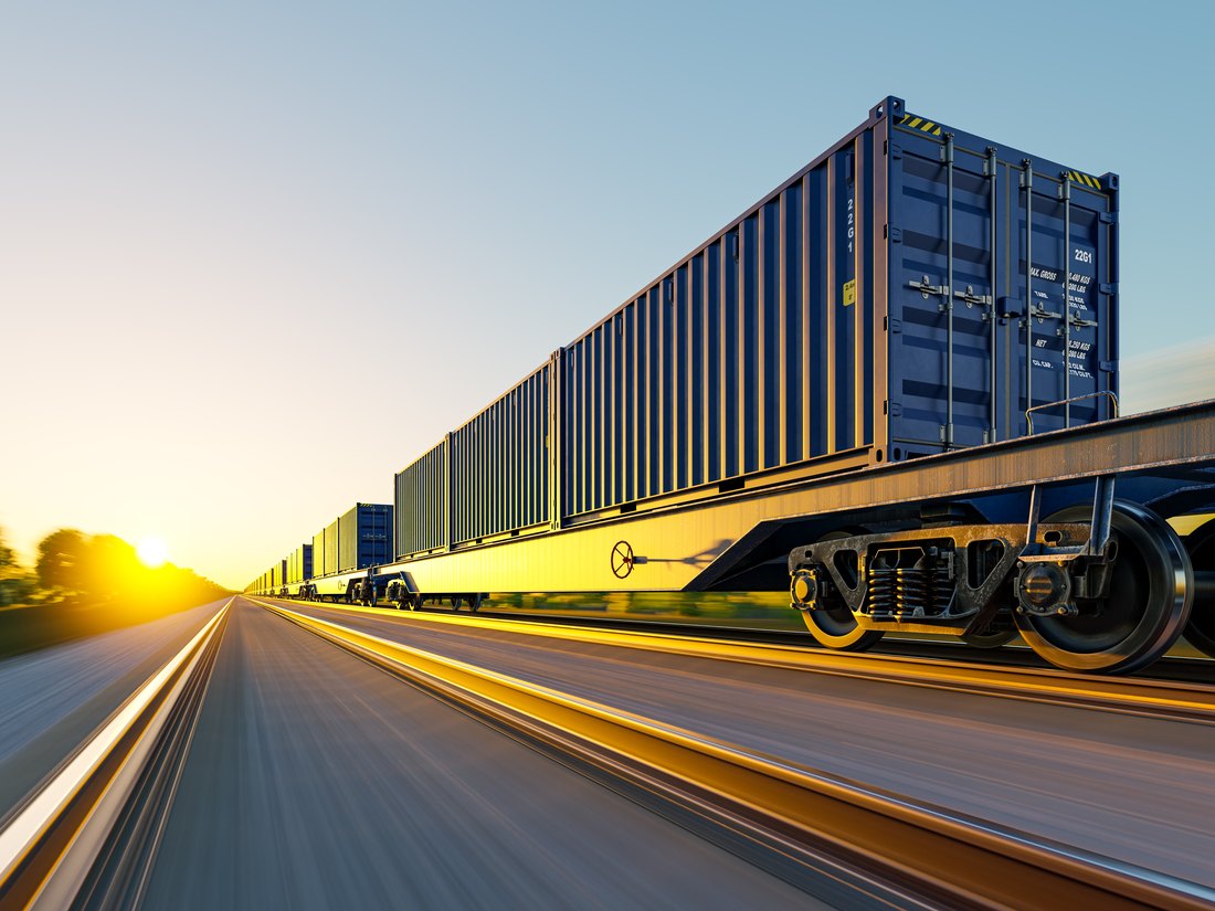 Low-angle view of a container freight train against a golden sunset